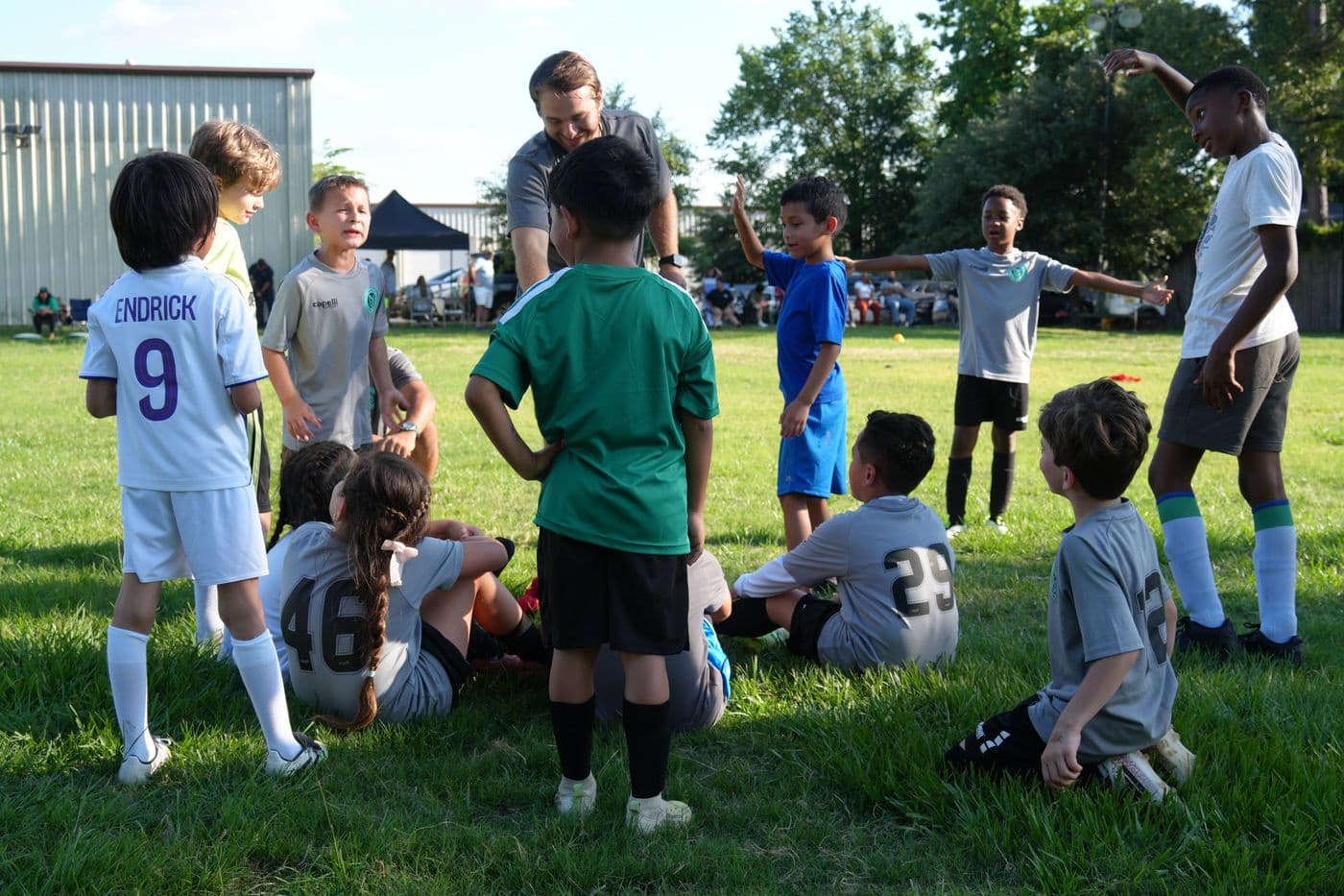 A NEXO coach leads a mixed group of young players through a warm-up on a grass field