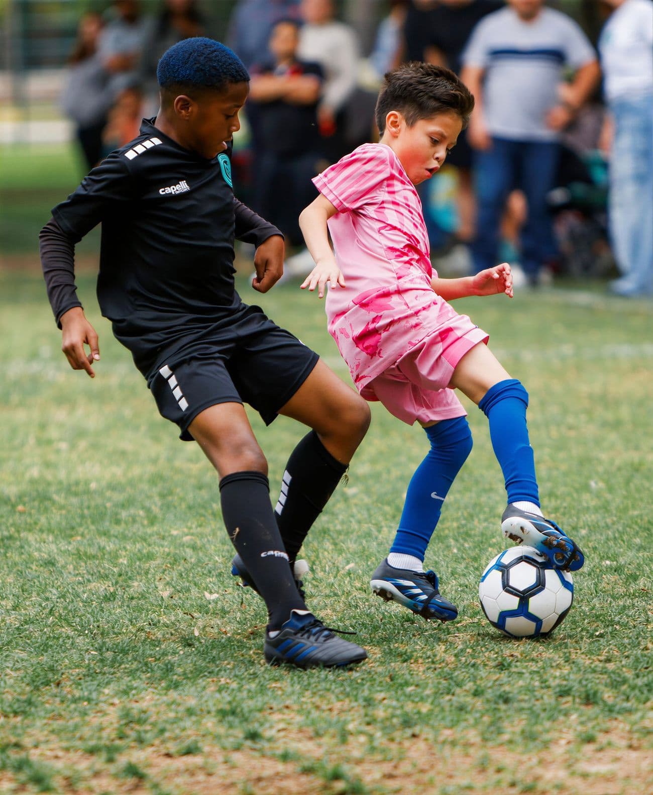 A NEXO player in the black club kit battles an opponent for the ball during a youth match